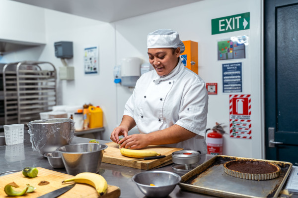 Student chef is preparing fruit on a chopping board.